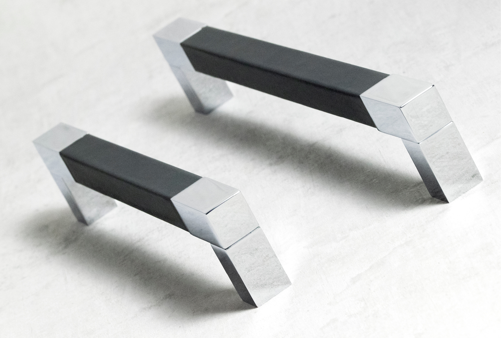 The image is of two square recess leather cabinet pull. The centre grip section is covered in black leather. Both legs are finished in bright chrome.