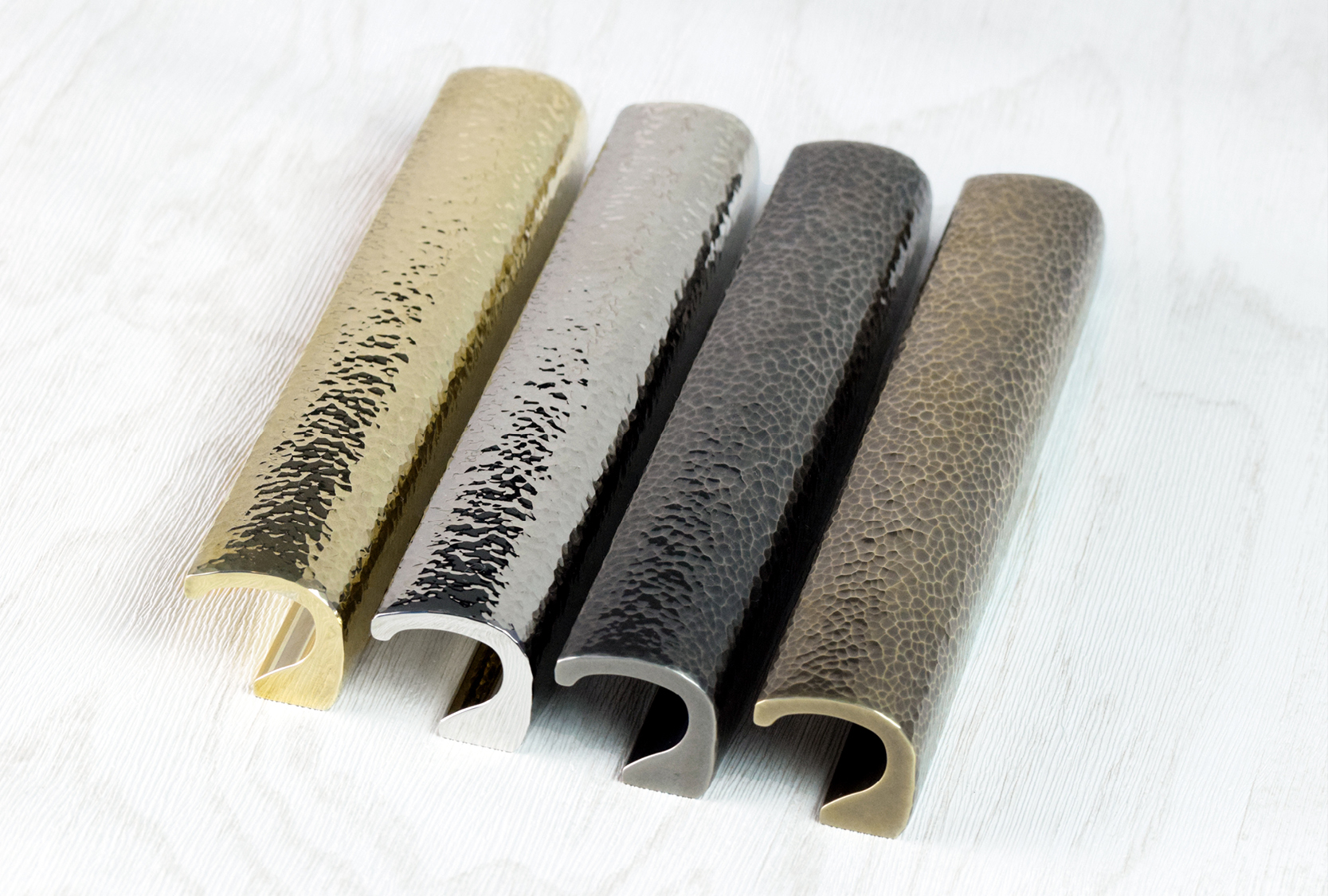 Image displays five custom length, echo solid hammered, cabinet pull. Each cabinet pull is displayed in a different variety of metal finishes. Hand hammered and crafted by Turnstyle Designs.