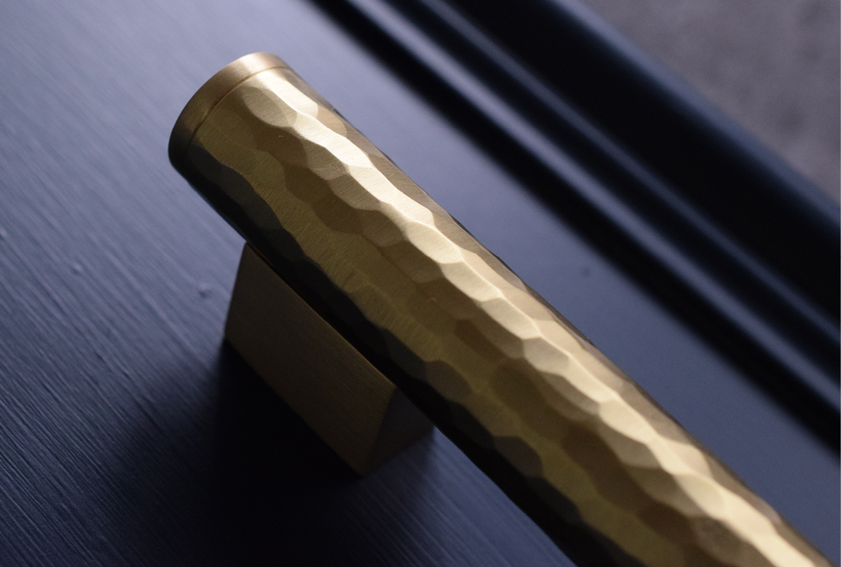 Coffin leg hammered solid scroll fixed to a navy cabinet door. The grip is hand hammered, finished in satin brass waxed.