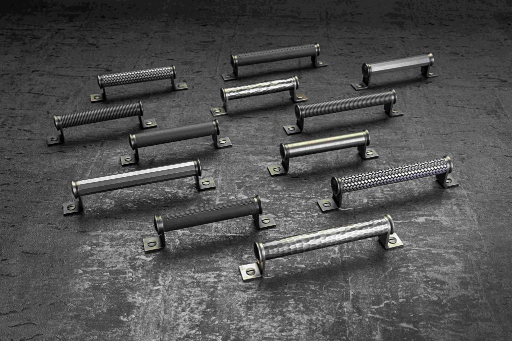 Designed by Christina Roberts, Turnstyles` new Bracket pull handles were inspired by a 1950’s vintage kitchen dresser Christina found in a local reclamation yard. A simpler principle of Turnstyles’ best-selling designs, was created with a chunkier grip. This includes hammered and solid brass, hand stitched leather, and their trademark Amalfine™ designs such as Wire, Faceted and Woven. These are all set between two L shaped brass brackets and finished with an elegant domed fixing. In this picture shows different finish combination bracket cabinet handles positioned in staggered lines. The brass finish used is Vintage Nickel, a dark grey moody colour.