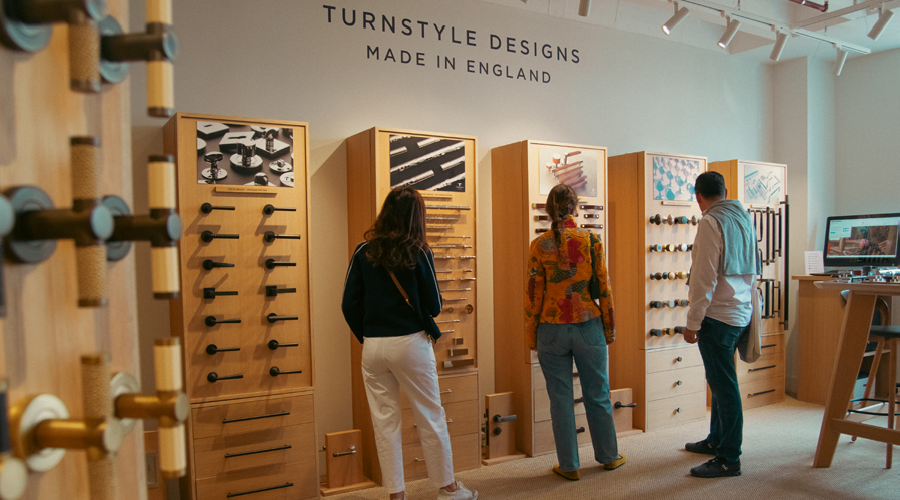 Three people stand in the Turnstyle Designs London showroom browsing the luxury door and furniture hardware on show.