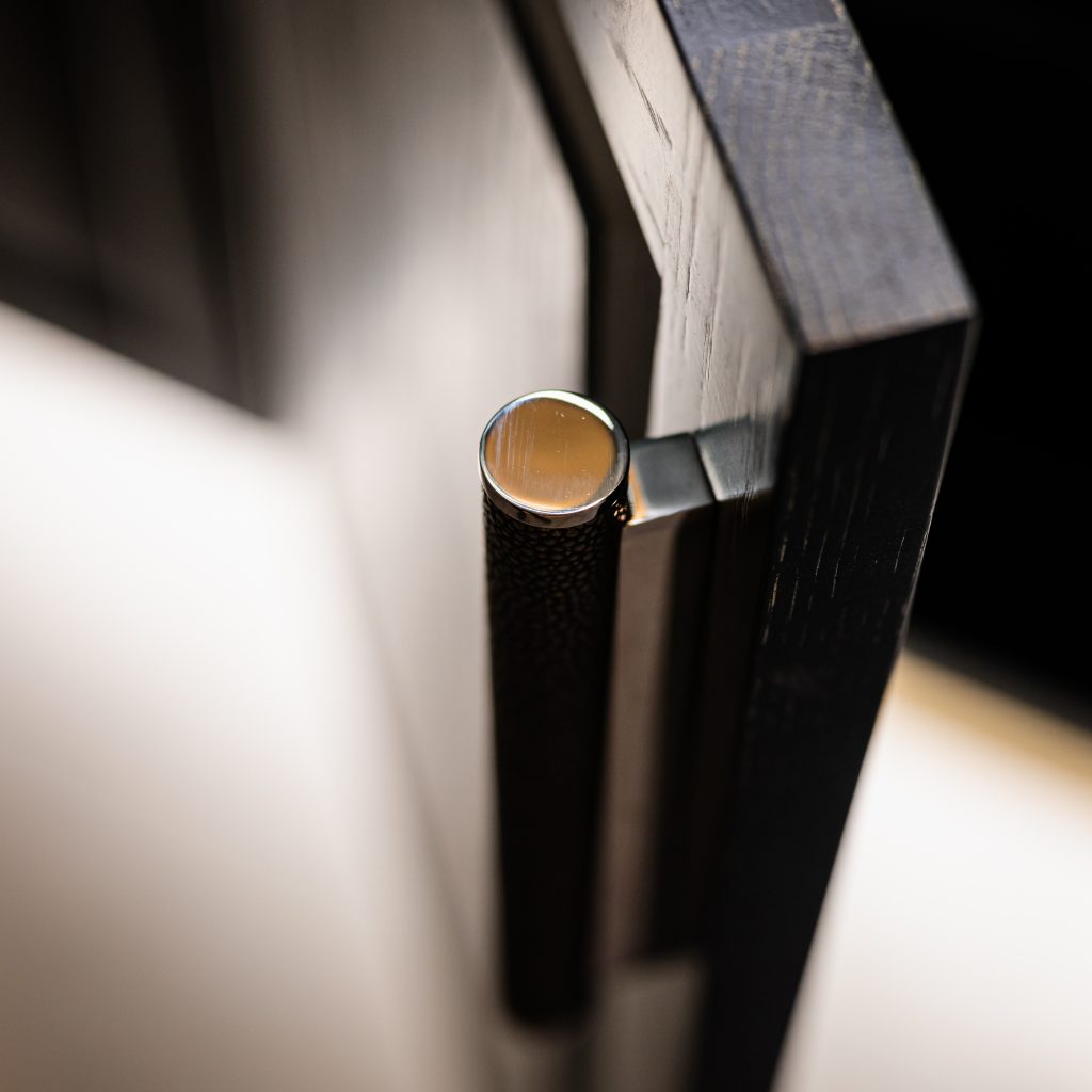 Turnstyle Designs Shagreen cabinet pull is shown here on this open cupboard door. The cupboard is a deep wooden finish, matching the dark grey hue of the cabinet pull grip.