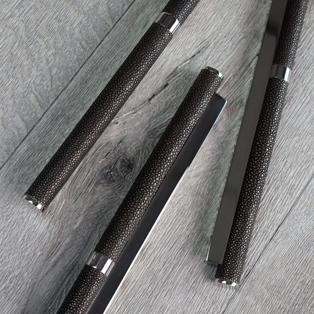 Unique custom cabinet hardware by Turnstyle designs is pictured. Lay on their sides, these scroll shaped handles have a custom central brass collar added to them to make them longer. The grip sections are finished in Alupewt and Polished Nickel. A deep grey hues with the reflective warm brass of the polished nickel.