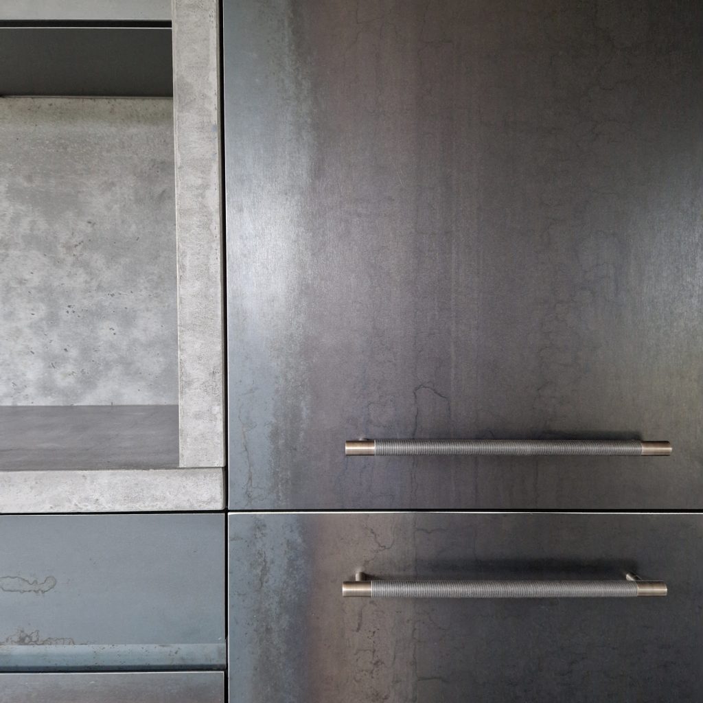 Wire design Amalfine cabinet pulls from Turnstyle Designs are used on a grey metal, cold but clean kitchen. The large cupabords shown here have handles attached horizontally.