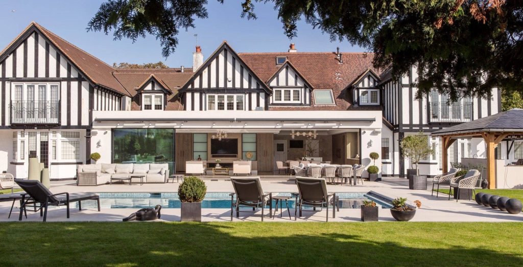 Large tudor property in Kent, United Kingdom. A swimming pool is in the foreground of the image before leading to a vast modern extension which includes a new kitchen and home bar set up.