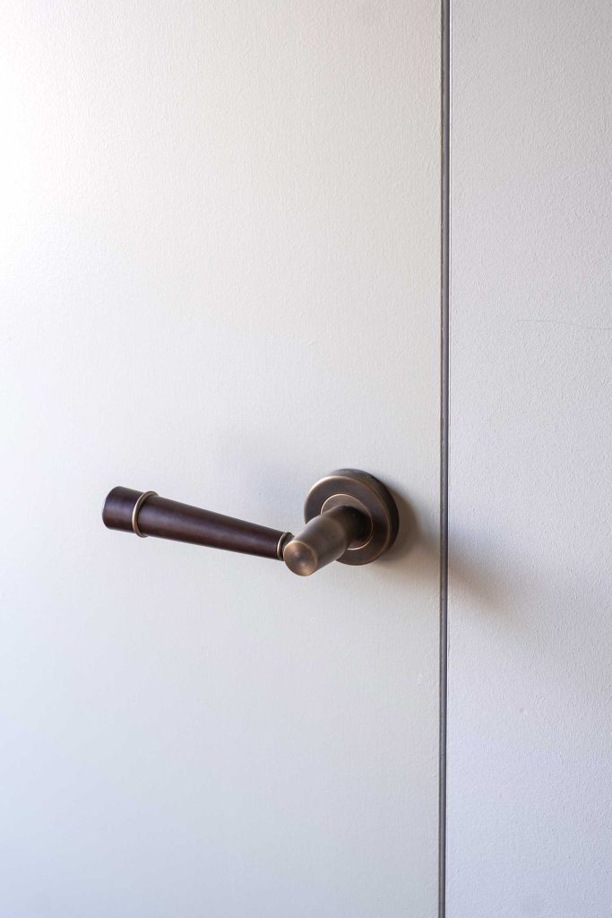 Luxury hand made door lever shown on a simple white painted door recessed into the wall. The door lever, designed by Turnstyle Designs, is a Flute design with a tapered grip and decorative brass ring.