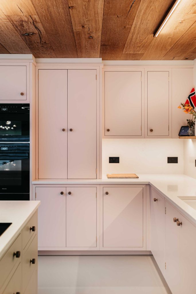 A contemporary soft pink kitchen with decorative wooden panelled ceiling. Hand hammered barrel shaped cabinet knobs are used for each cabinet door, these have been hand made by Turnstyle Designs.