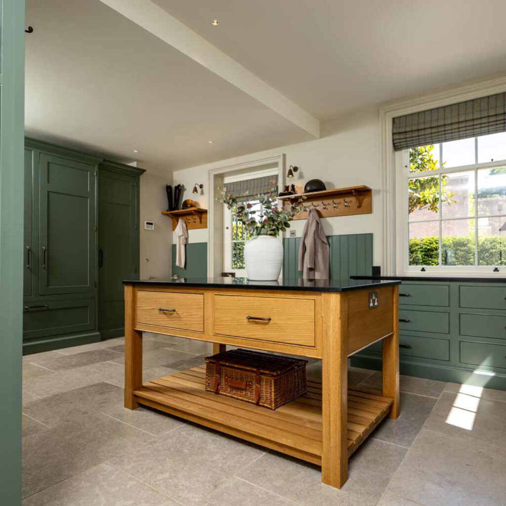 Large oak island sits in the centre of this large luxury utility/boot room. Finished with green cabinetry, Turnstyle Designs leather cabinet handles and black quartz work tops.