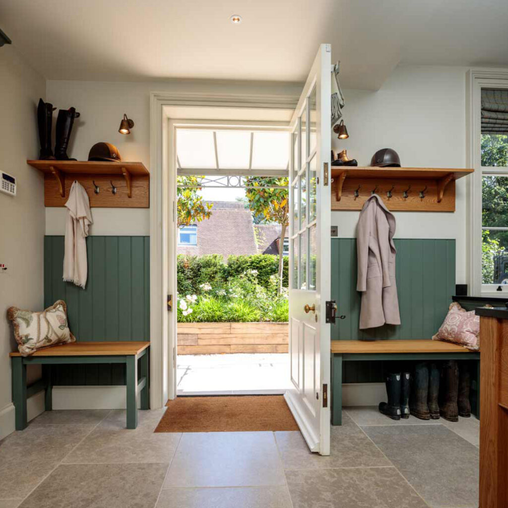 Looking through an open door to a sun filled garden from inside a large spacious utility room. Decorative wooden panelling in Farrow and ball, Green Smoke is used alongside light coloured oak wood.